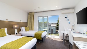 Ein Hotelzimmer mit zwei Betten, einem Schreibtisch und einem Balkon mit Glastür.
