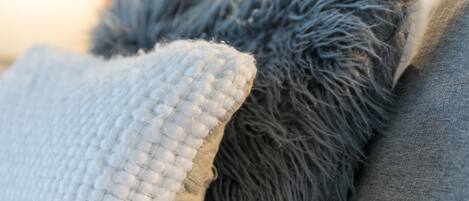A bed with a white textured pillow and a fluffy gray pillow.