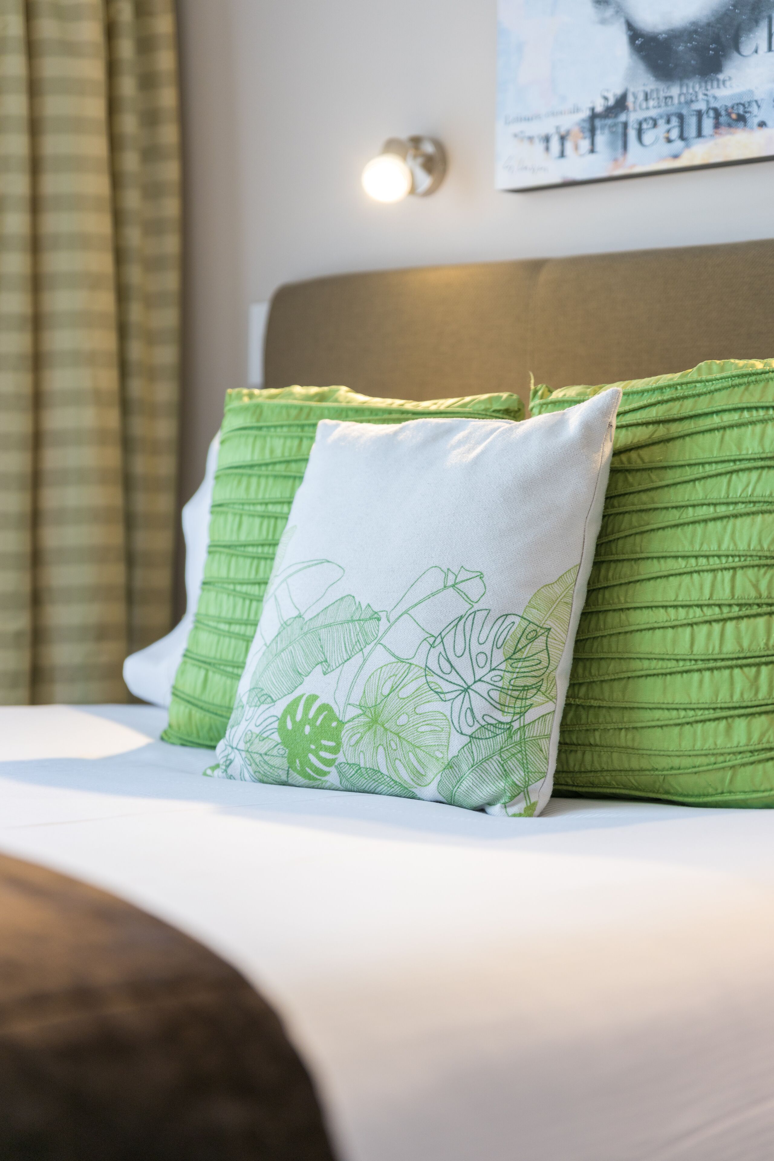 Una cama con almohadas verdes y blancas, un cabecero y una pared con un cuadro enmarcado.