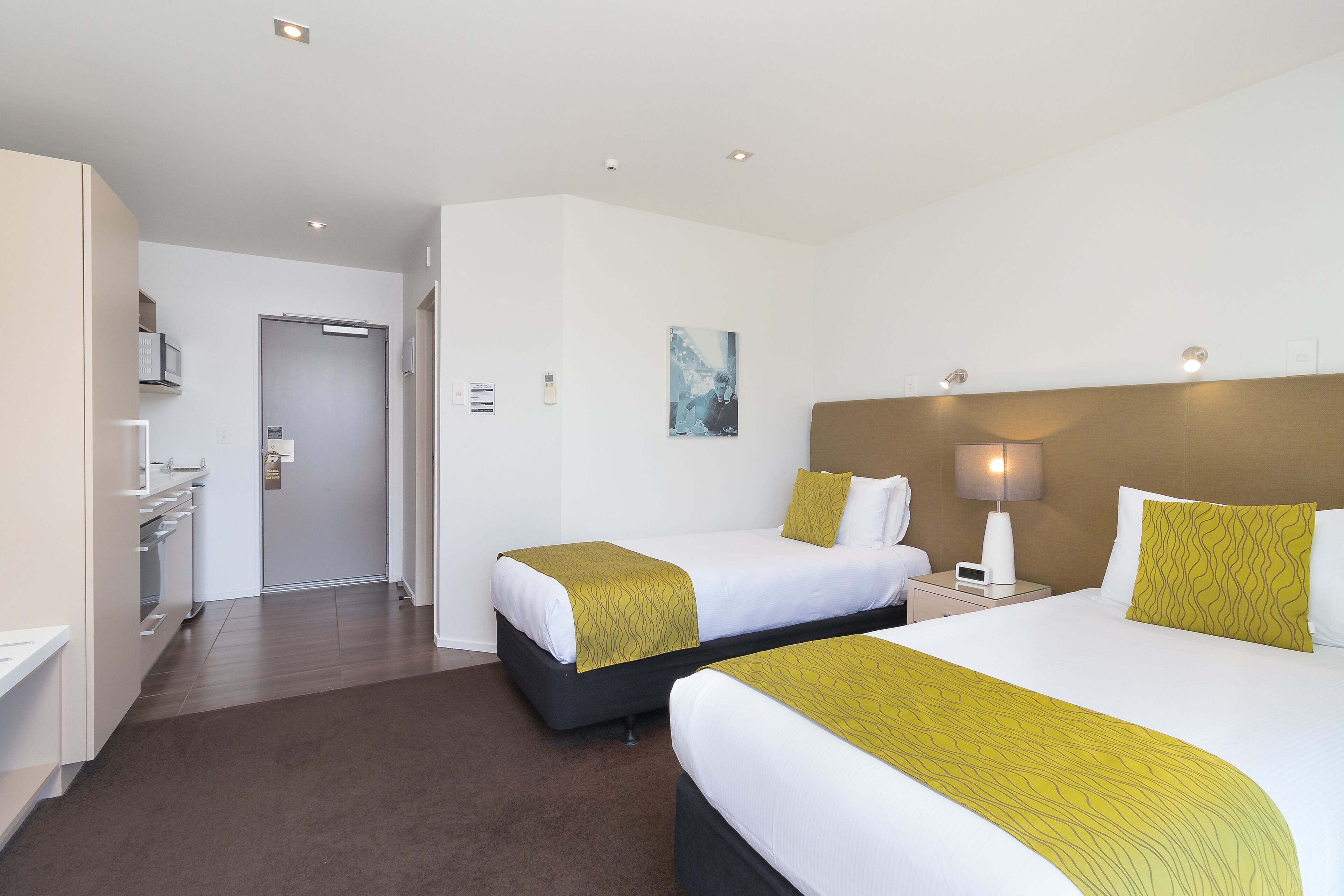 A hotel room with two beds, a desk, a chair, a lamp, and a painting on the wall.