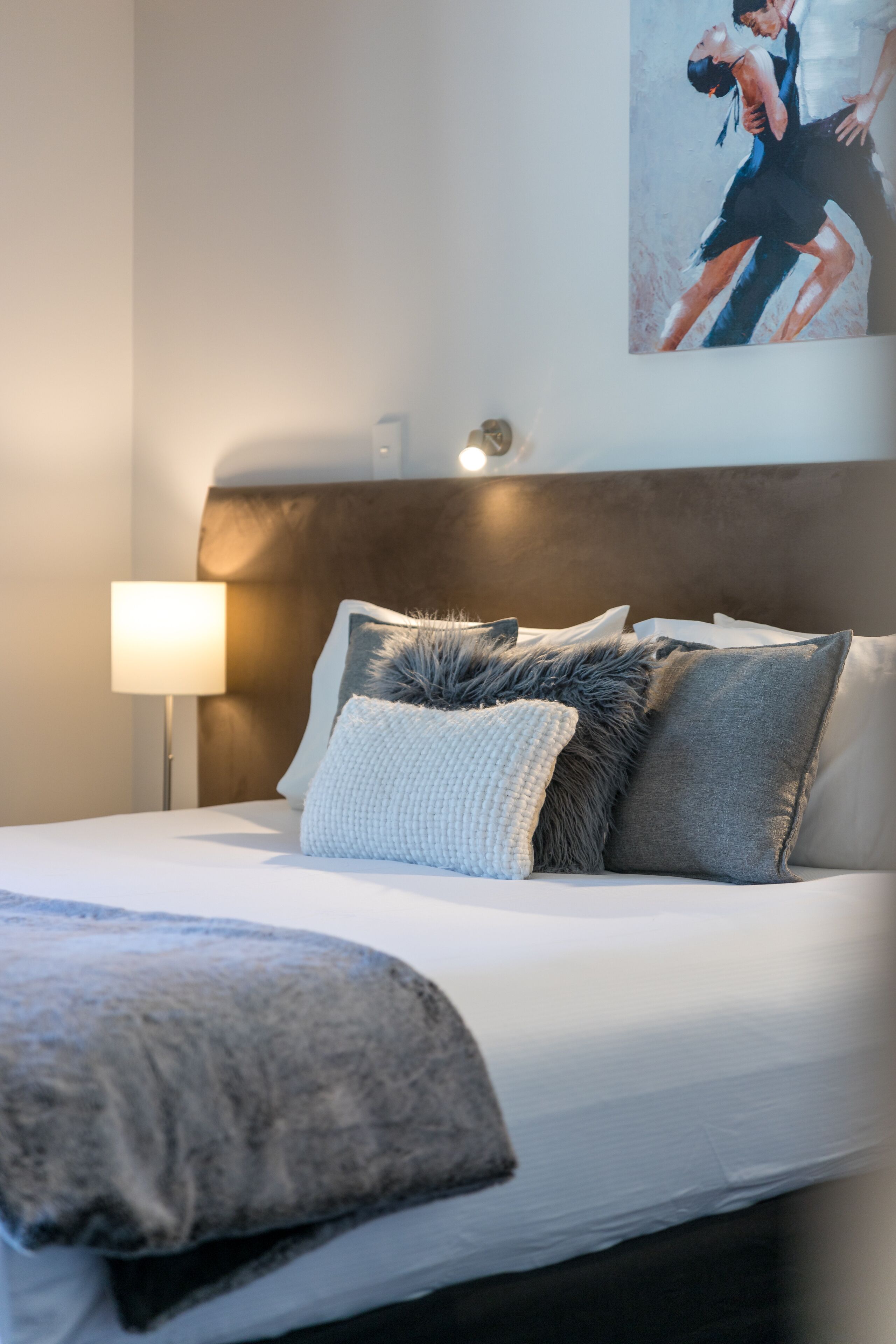 Un lit bien fait, avec un oreiller moelleux, une lampe de chevet et un tableau accroché au mur.