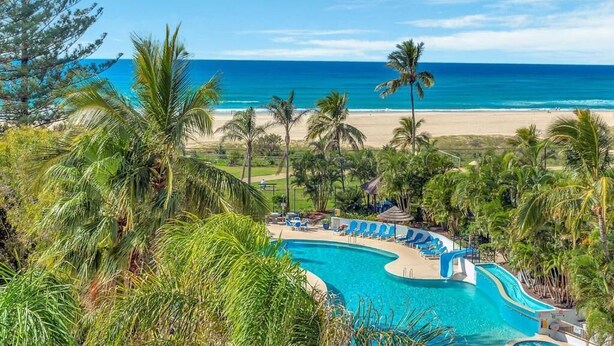 Une piscine d’hôtel à bordures incurvées, entourée de palmiers et offrant une vue sur la plage.