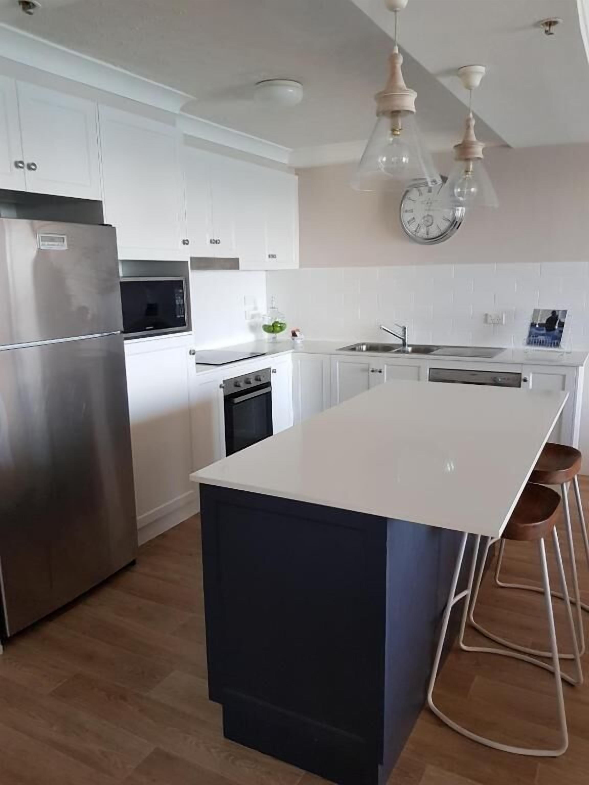 A modern kitchen with white cabinetry, stainless steel appliances, a central island with stools, and pendant lighting.