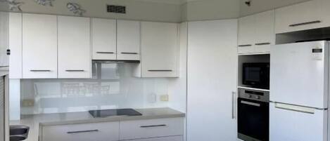 Una cuina moderna amb armaris blancs, una illa central i electrodomèstics integrats, com ara un frigorífic, un forn i un microones.