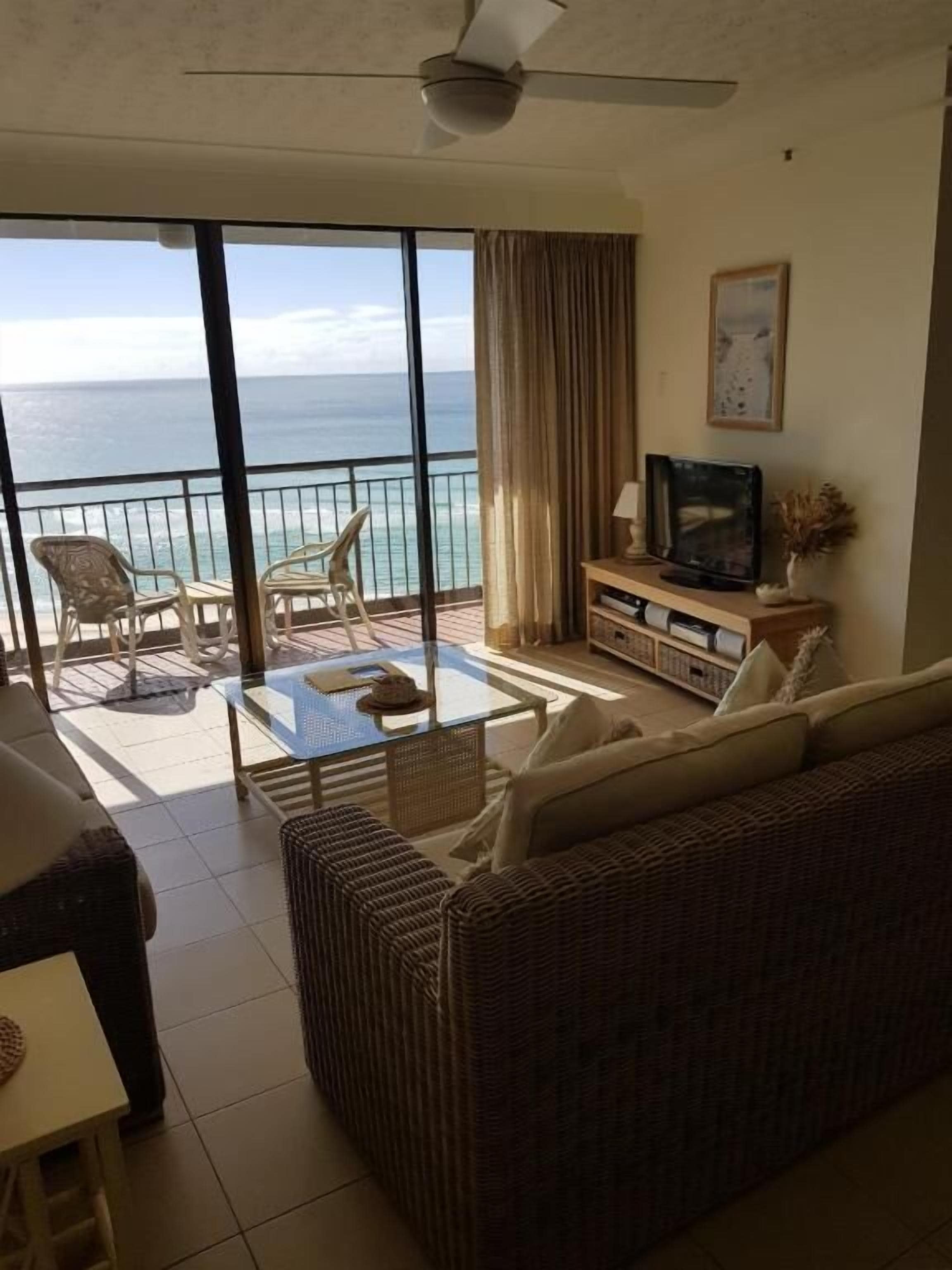 Ein Wohnzimmer mit einer Couch, einem Couchtisch und einer TV-Konsole. Es gibt einen Balkon mit Meerblick.