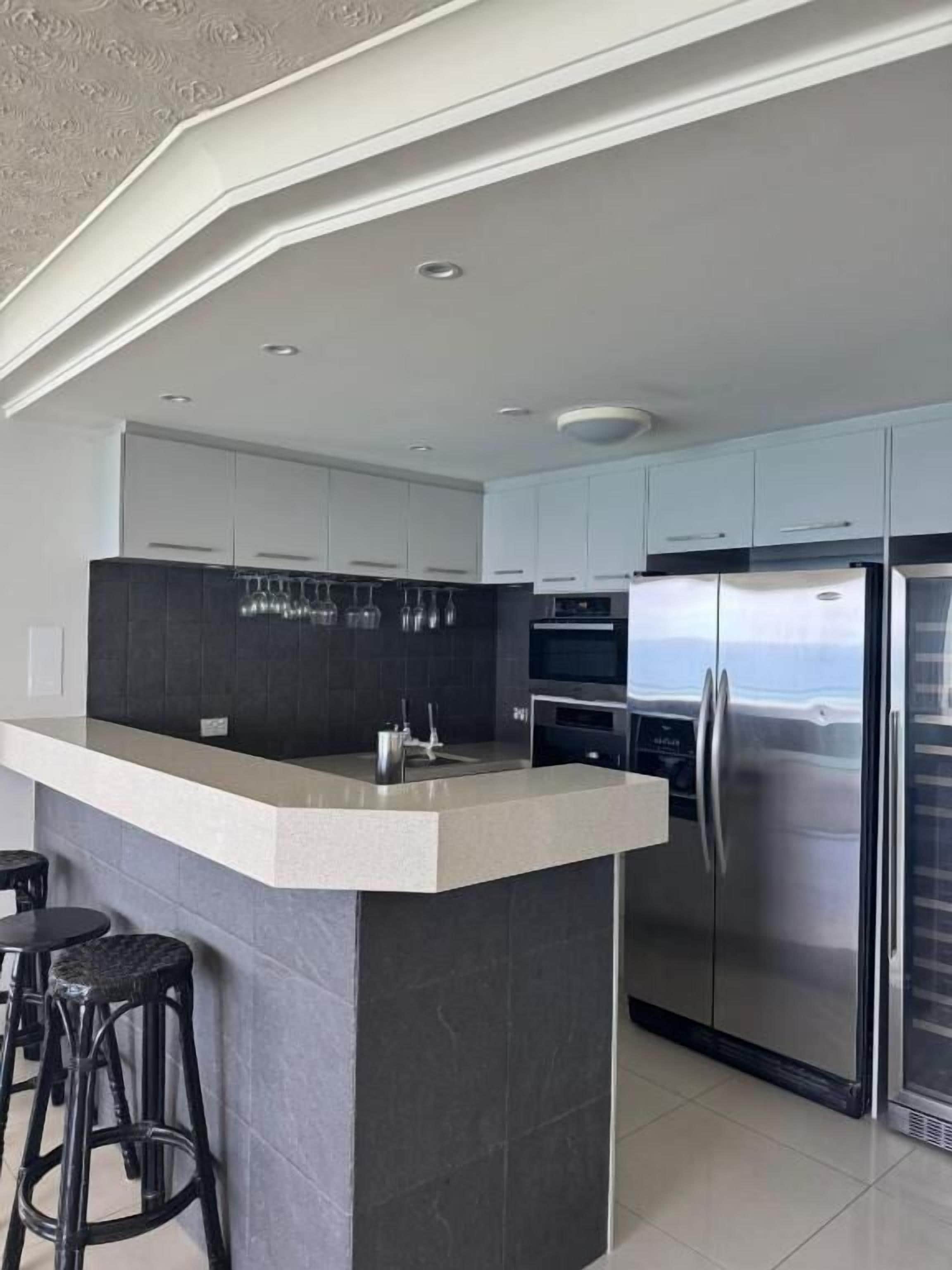 Una cocina moderna con una isla central, electrodomésticos de acero inoxidable y salpicadero de azulejos oscuros.