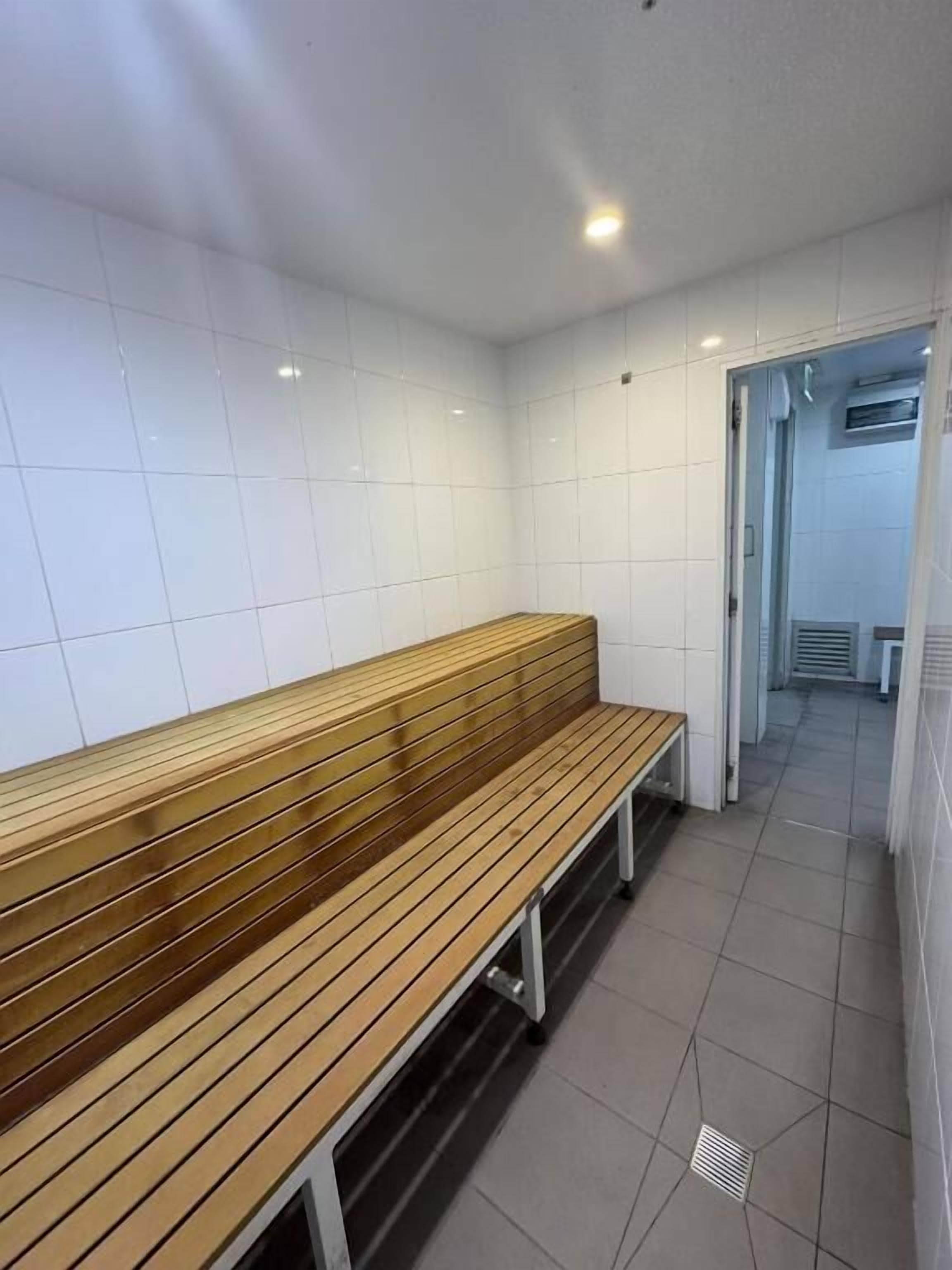 A clean, tiled bathroom with a wooden bench and a shower area visible through an open door.