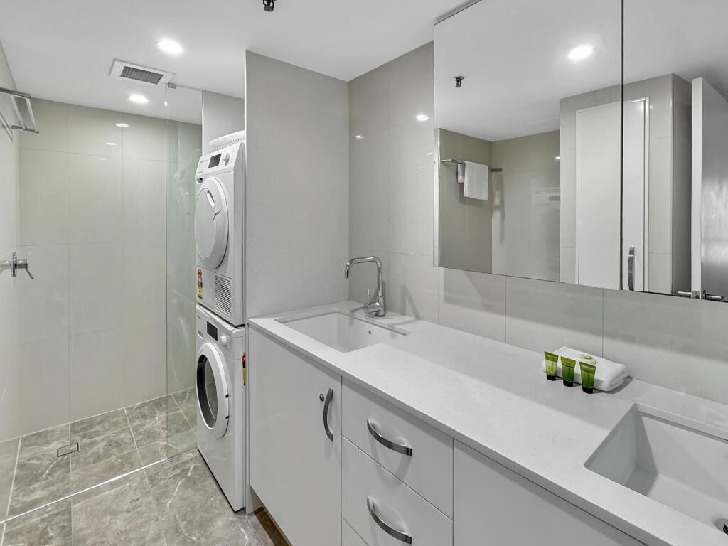 A modern bathroom with a large mirror, a sink, and a washing machine.