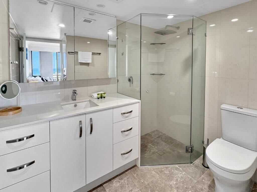 A modern bathroom with a glass-enclosed shower, a white sink with a mirror, and a toilet.