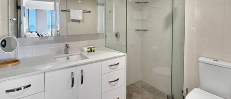 A modern bathroom with a glass-enclosed shower, a white sink with a mirror, and a toilet.