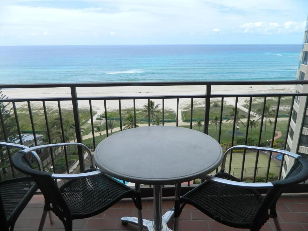 A balcony with a round table and two chairs, overlooking a beach and ocean.