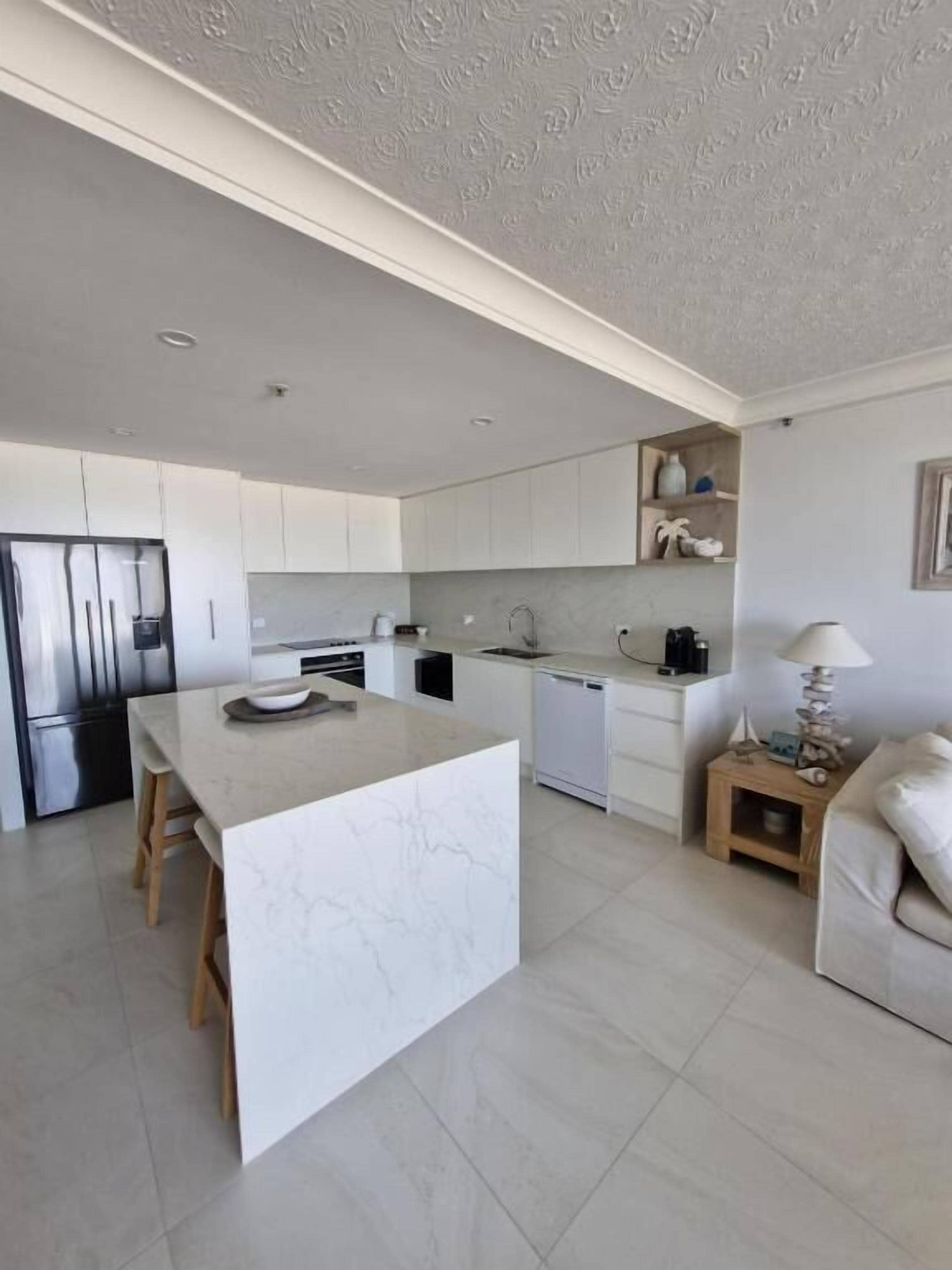 Cocina moderna con armarios blancos, una isla de mármol y lavavajillas integrado.