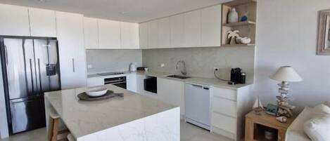 Cocina moderna con armarios blancos, una isla de mármol y lavavajillas integrado.