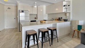 Une cuisine moderne avec des meubles blancs, un îlot central doté de tabourets et un réfrigérateur encastré.