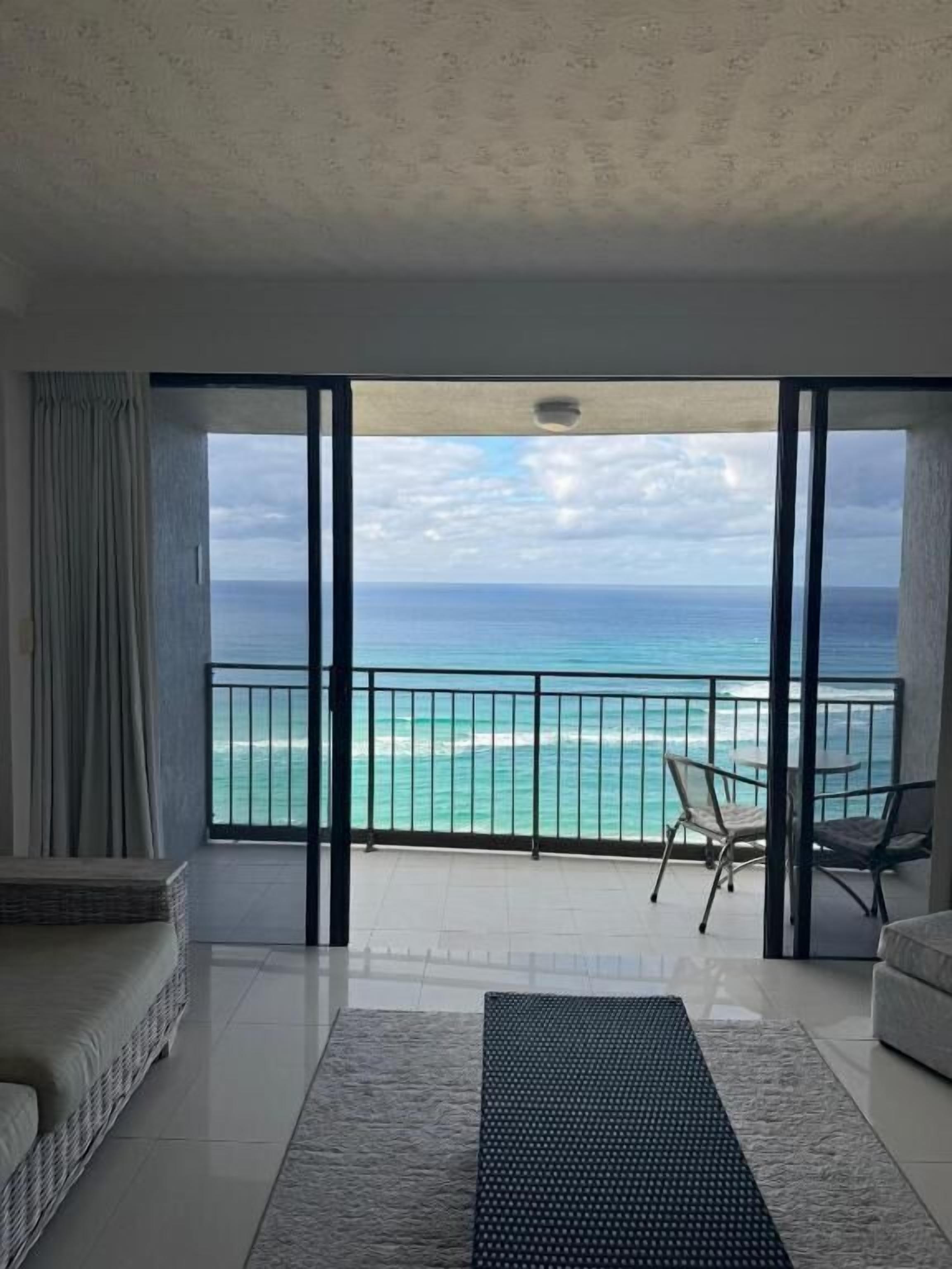 A room with a large sliding glass door leading to a balcony with a view of the ocean.