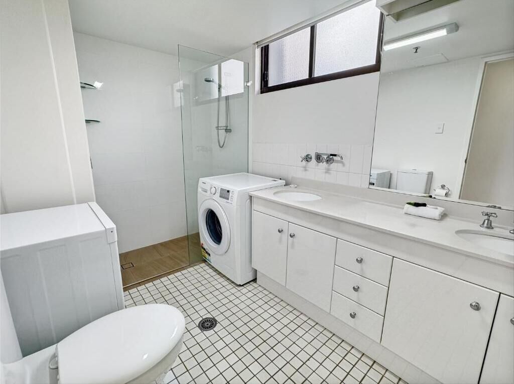 A modern bathroom with a toilet, washing machine, sink, and mirror.
