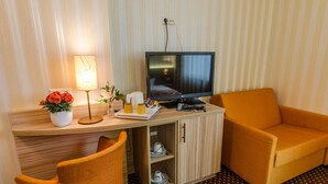 A hotel room with a wooden desk, a television, a lamp, a flower vase, a coffee maker, and a sofa. - Alte Post (Lehrte)