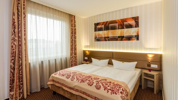 A hotel room with a large bed, two bedside tables, a wall-mounted artwork, and a window with curtains. - Alte Post (Lehrte)