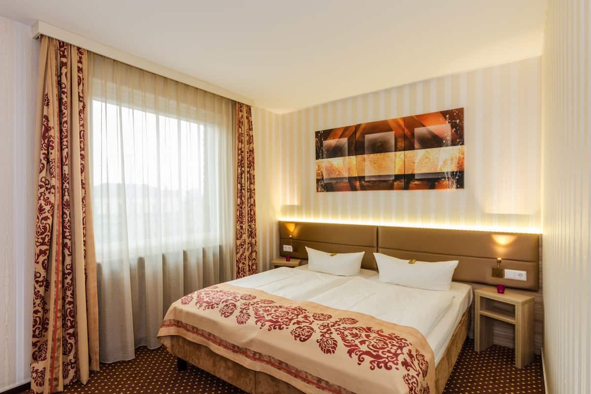 Een hotelkamer met een groot bed, twee nachtkastjes, een aan de muur hangend kunstwerk en een raam met gordijnen.