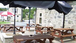 Outdoor wooden picnic tables with black umbrellas, set against a stone building backdrop. - The Glen Hotel (Newtonmore)