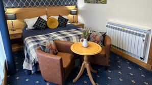 A bedroom with a bed, two nightstands, a table, a chair, a radiator, and a wall-mounted picture. - The Glen Hotel (Newtonmore)
