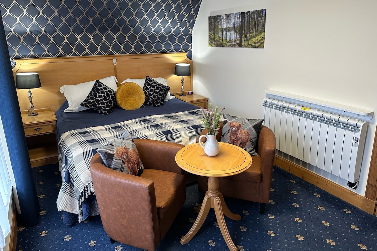 A bedroom with a bed, two nightstands, a table, a chair, a radiator, and a wall-mounted picture.