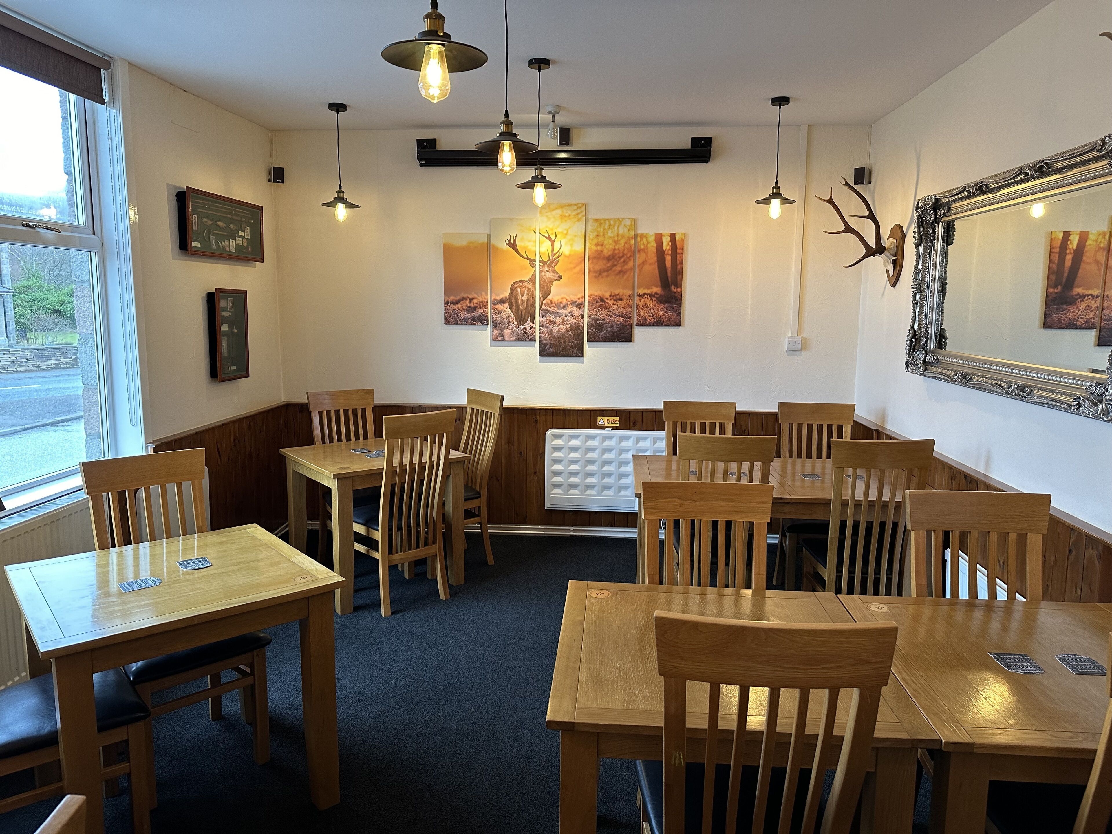 A restaurant with wooden tables and chairs, pendant lighting, and wall art.