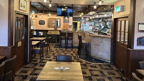 A bar area with a wooden bar counter, multiple seating options, and a patterned carpet. - The Glen Hotel (Newtonmore)