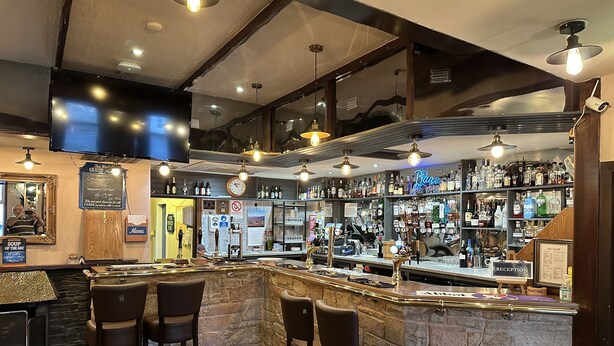 A bar area with a stone counter, bar stools, and a variety of liquor bottles. - The Glen Hotel (Newtonmore)