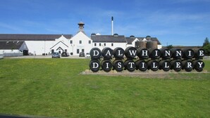 A distillery with barrels labeled "DALWHINNIE DISTILLERY" and a white building in the background. - The Glen Hotel (Newtonmore)