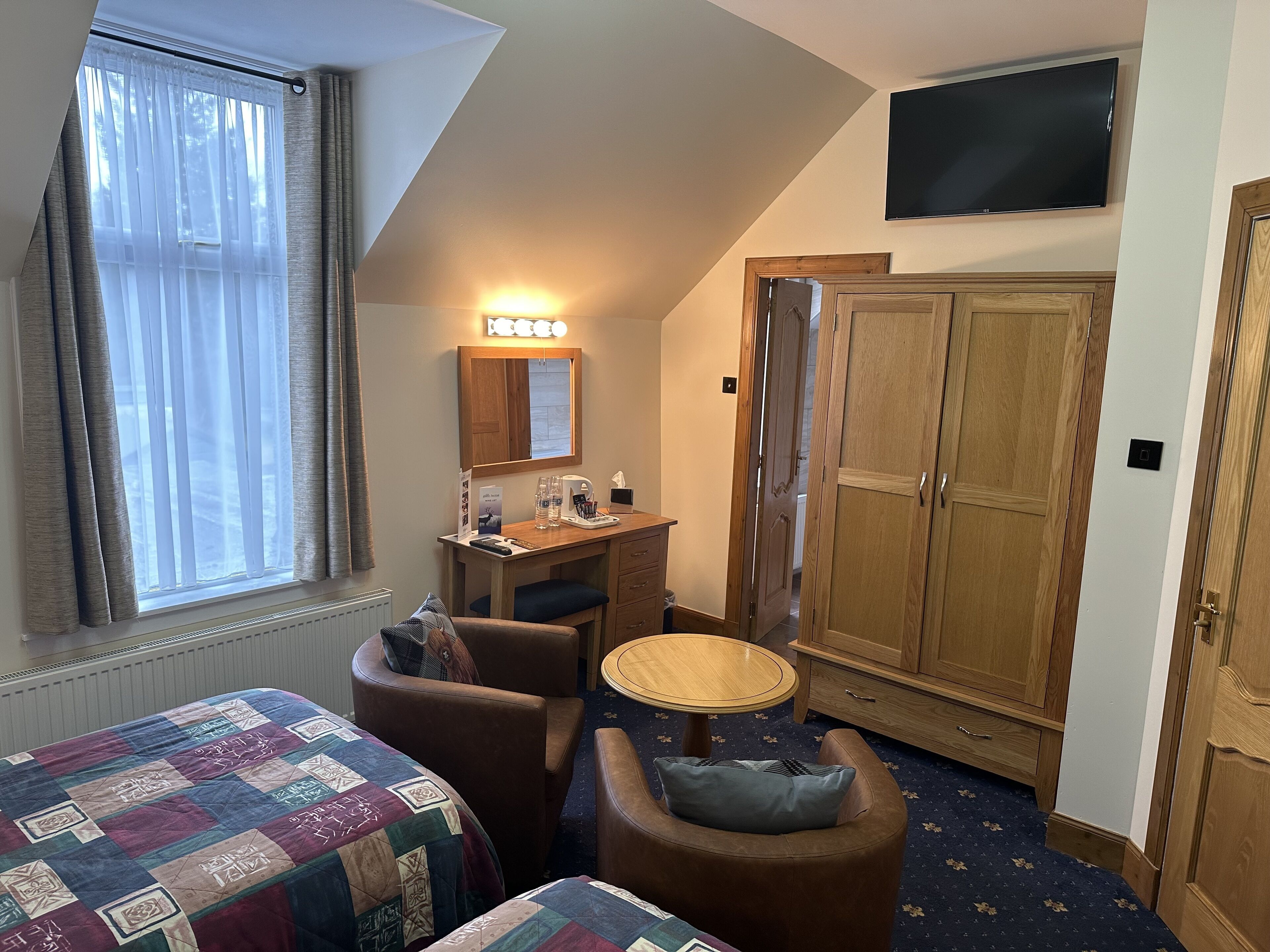 A hotel room with a bed, a desk with a mirror, a television, and a wardrobe.