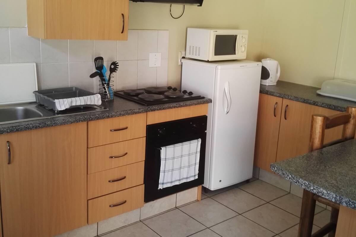 A compact kitchen with wooden cabinets, a microwave, a stove, and a refrigerator.