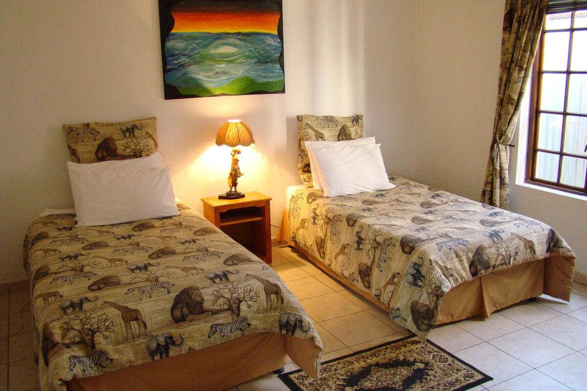 A room with two beds, a painting on the wall, a lamp, and a window with curtains.