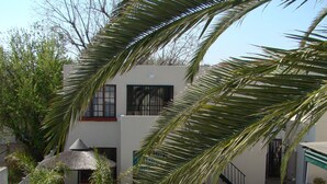 A swimming pool with a black metal railing, surrounded by greenery and a building with a white facade and a black gate.