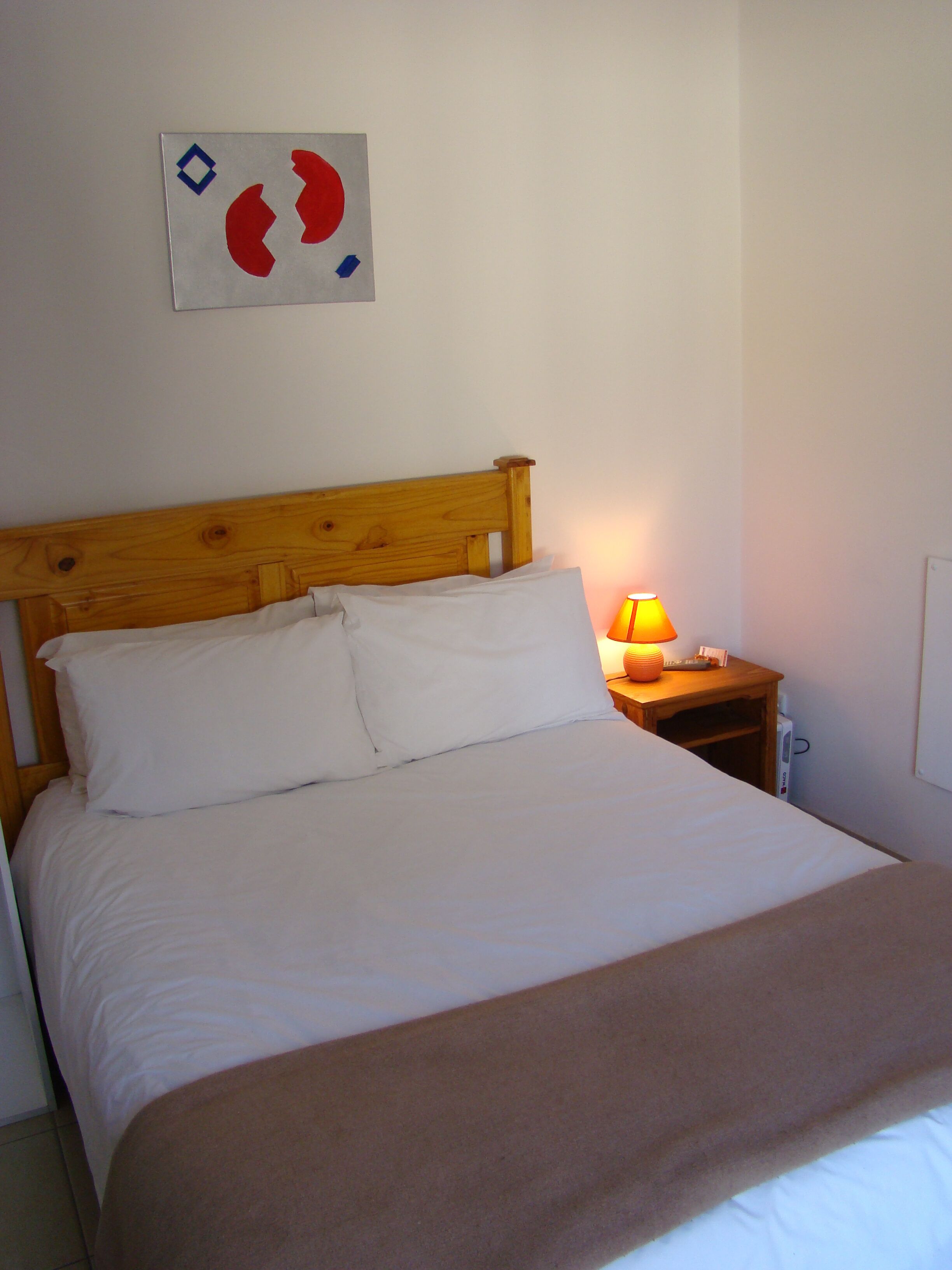 A neatly made bed with white linens, a wooden headboard, and a bedside table with a lamp.