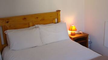A neatly made bed with white linens, a wooden headboard, and a bedside table with a lamp.