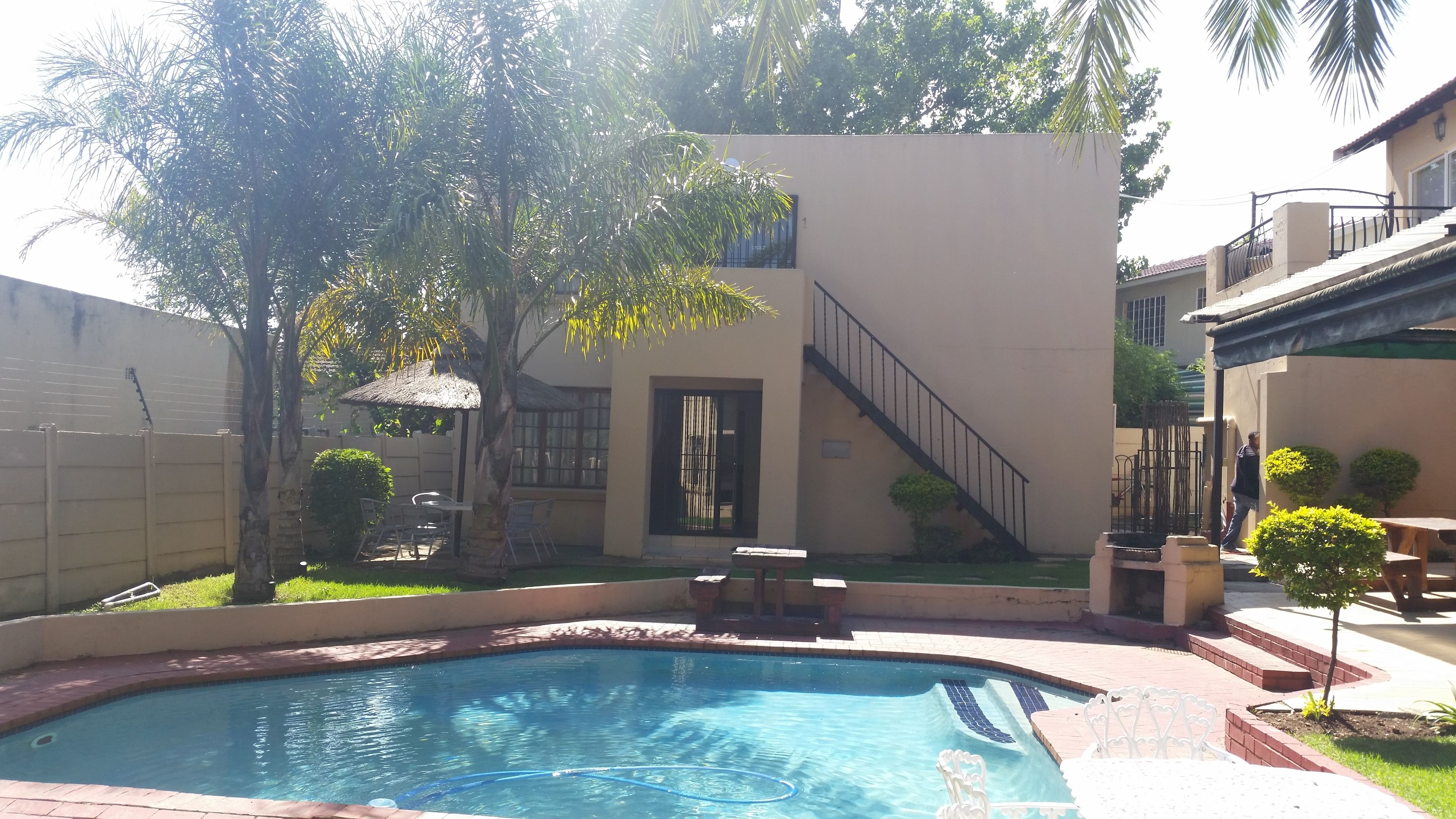 Una piscina con borde de azulejos, un área de patio techada con sillas y una escalera que lleva a un segundo piso.