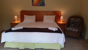 A neatly made bed with white and green bedding, two bedside lamps, and a chair with a patterned cushion.