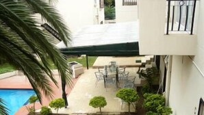 A residential outdoor area with a swimming pool, a covered patio with chairs, and a small garden.