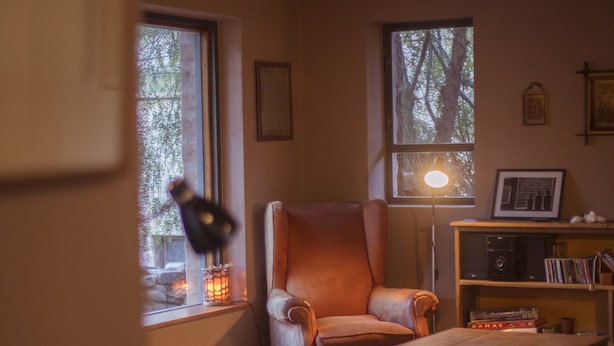 A cozy room with a wooden ceiling, a leather armchair, a small table, a bookshelf, and a window with a view of trees. - Patio Alto (Tilcara)