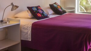A bedroom with a bed, pillows, a nightstand, a lamp, and a window. - Patio Alto (Tilcara)