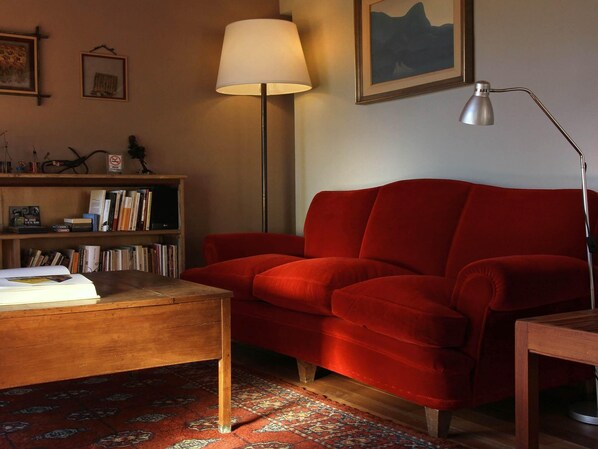 A cozy living room with a red sofa, a wooden coffee table, a floor lamp, and a bookshelf filled with books.
