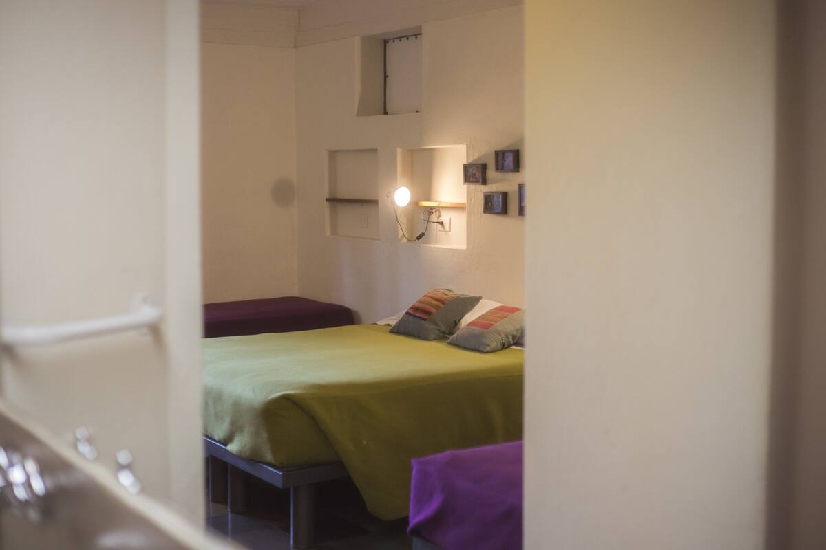 Un dormitorio pequeño y bien iluminado con cama, una mesita de noche y una lámpara fijada a la pared.