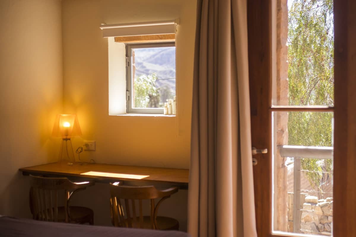 Una habitación con escritorio, dos sillas, lámpara y ventana con cortinas.