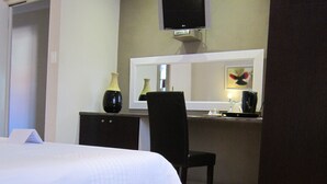 A bedroom with a bed, a desk, a chair, a television, and a mirror. - La Roche Guest House (Cape Town)