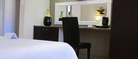 A bedroom with a bed, a desk, a chair, a television, and a mirror.