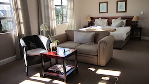 A hotel room with a sofa, a chair, a small table with magazines, a bed with pillows, and two framed pictures on the wall. - La Roche Guest House (Cape Town)