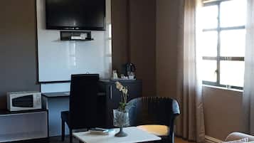Sala de estar com televisão de tela plana na parede, uma mesa pequena com um vaso de flores, um sofá, uma poltrona e um micro-ondas no chão.