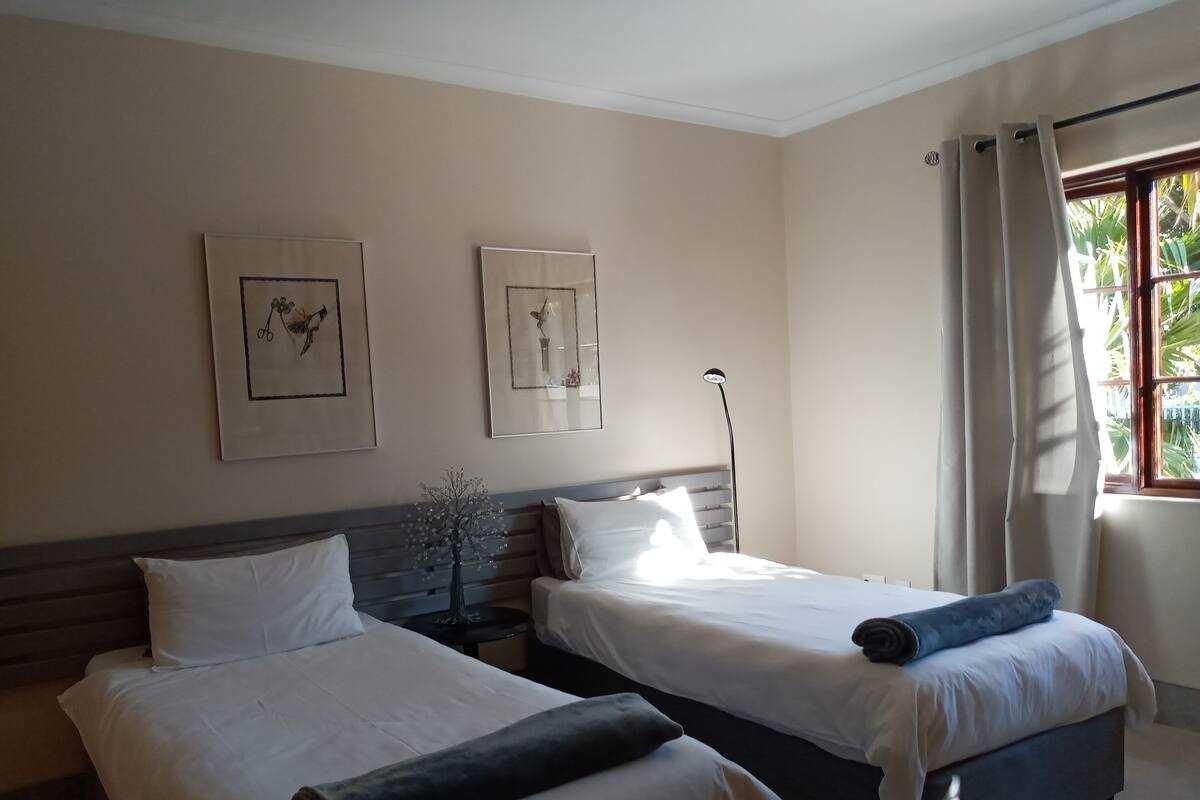 Habitación de hotel con dos camas, una mesita de noche, una lámpara y cuadros en la pared.