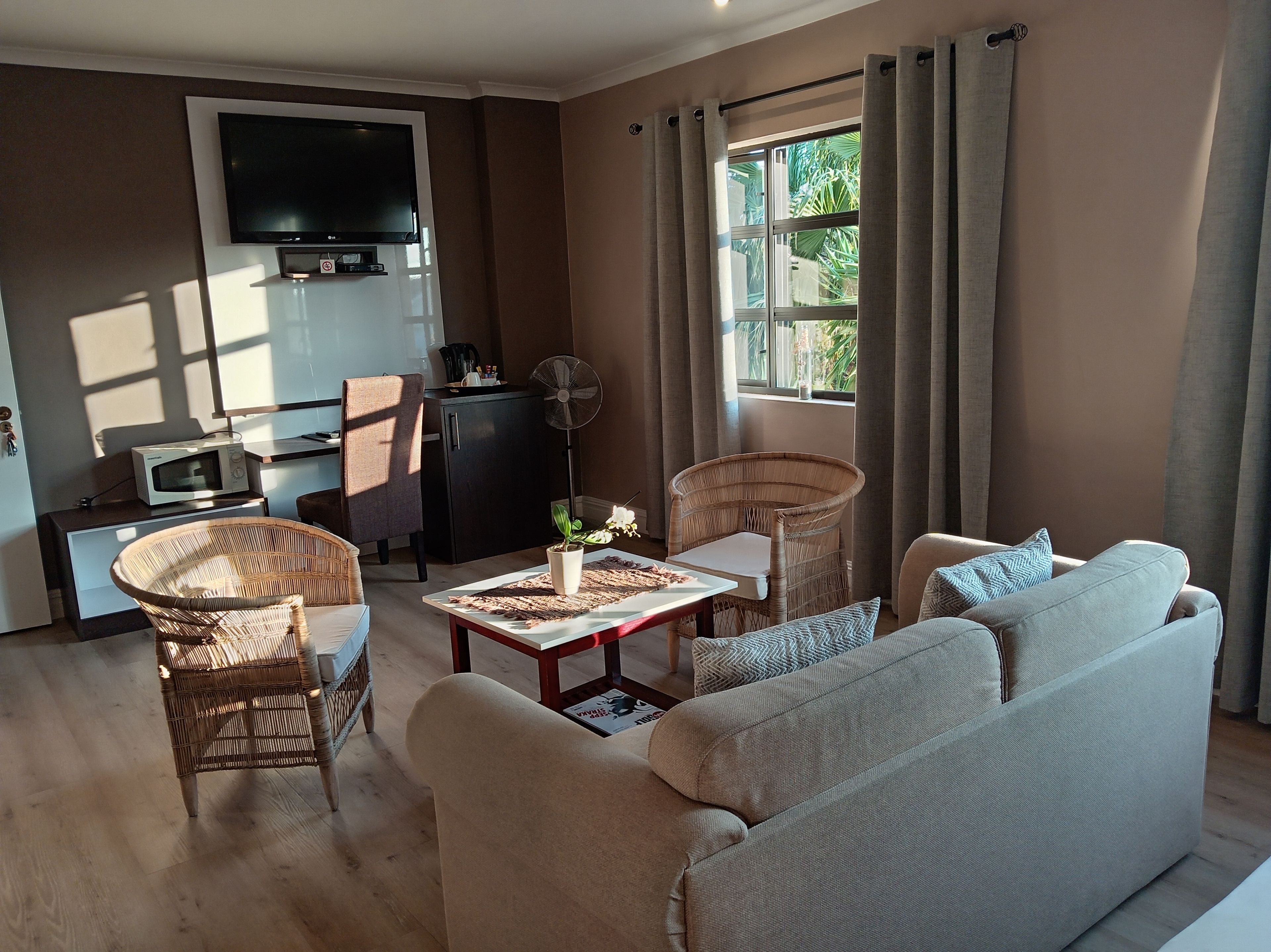 A living room with a sofa, two wicker chairs, a coffee table, a flat-screen TV, a microwave, and a small cabinet.